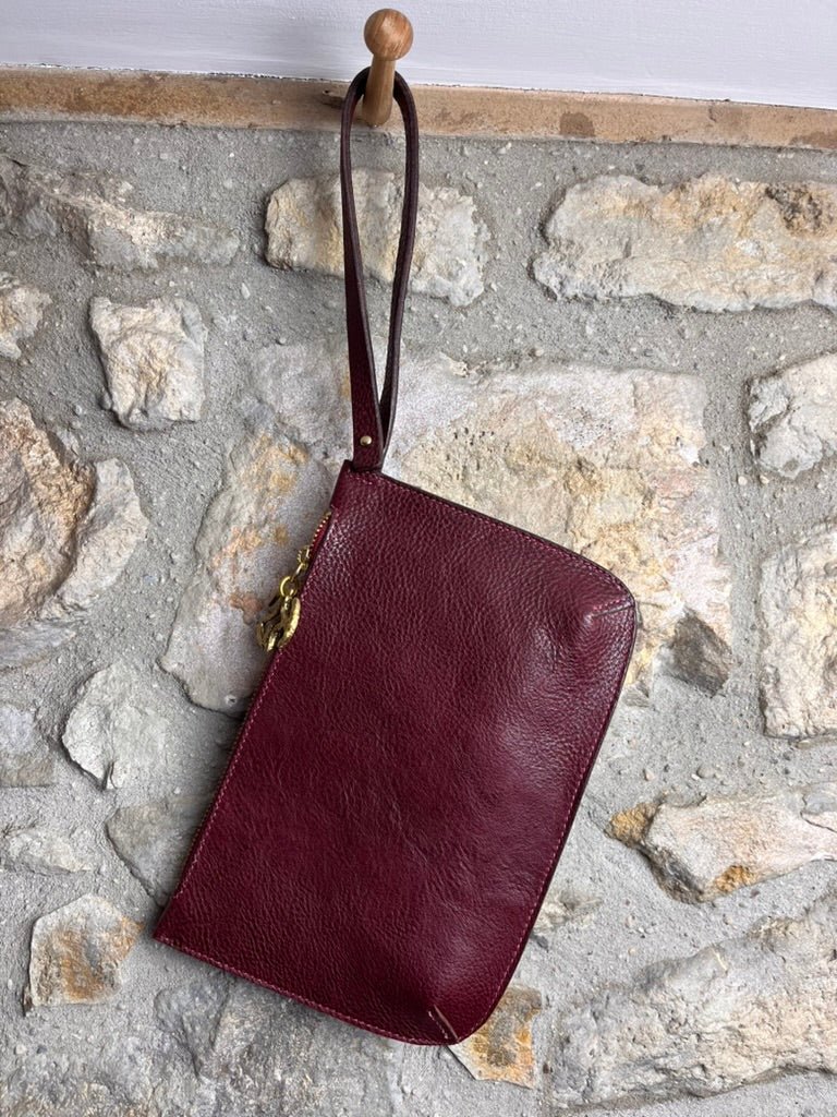 Zip pouch in burgundy veg tanned leather hanging on a stone wall Keep - Studio