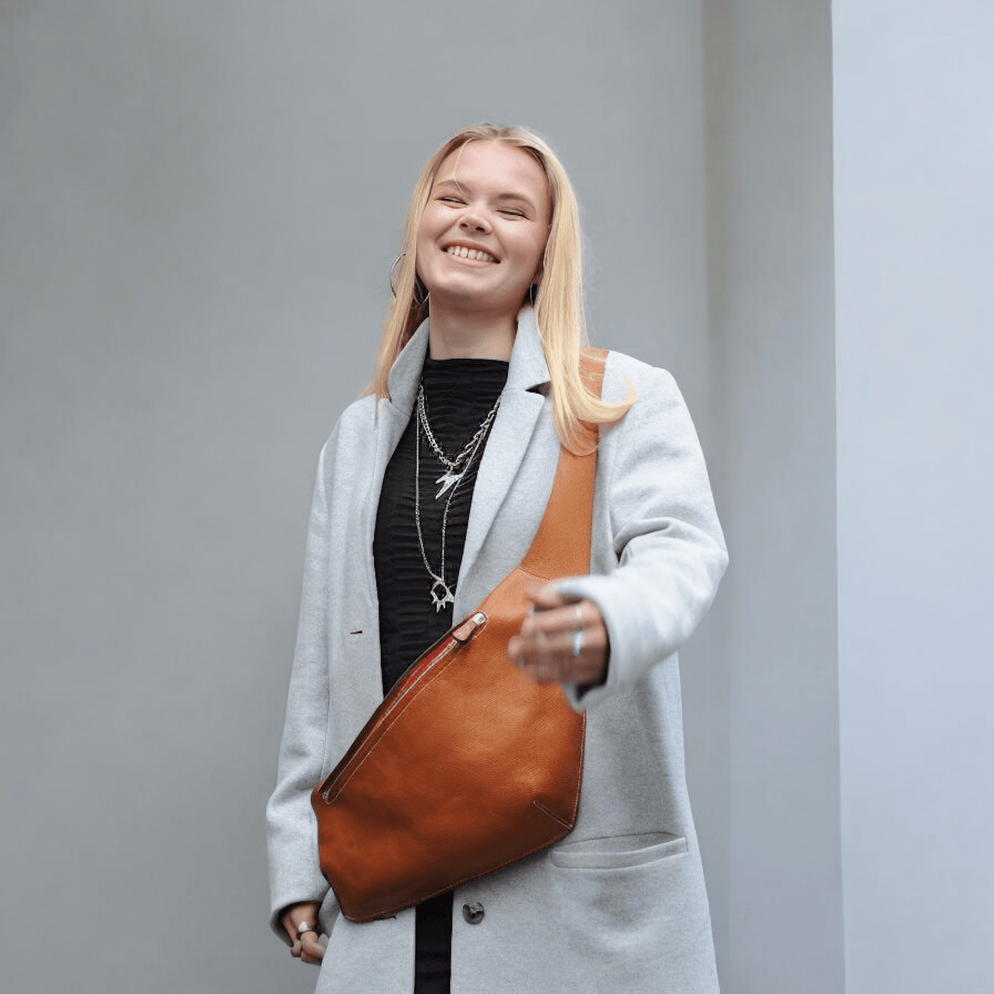 model wearing a grey coat and ther elron cross body bag by keep studio in tan with red zip