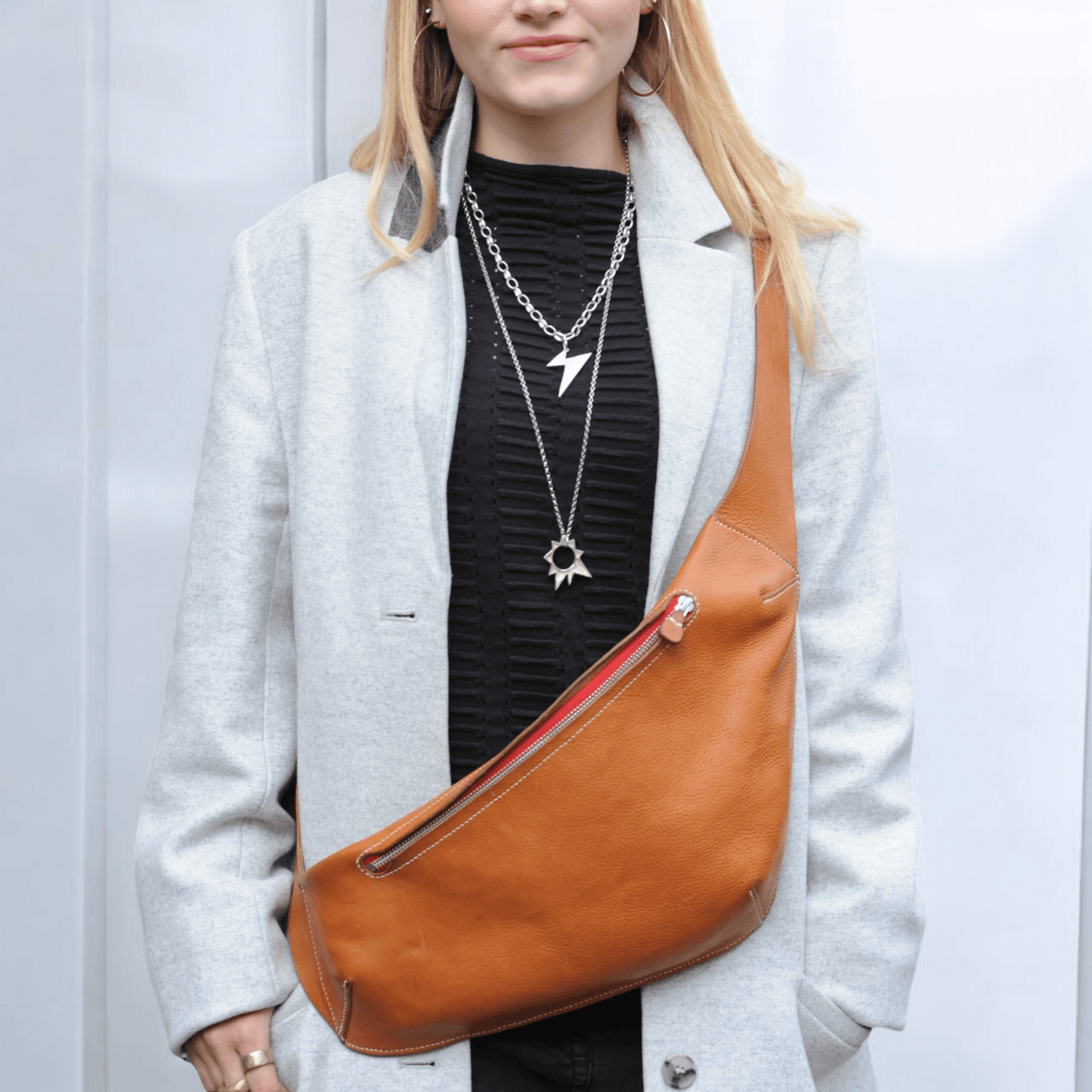 Handmade large asymmetric leather cross body bag on a model in light tan with a red zip