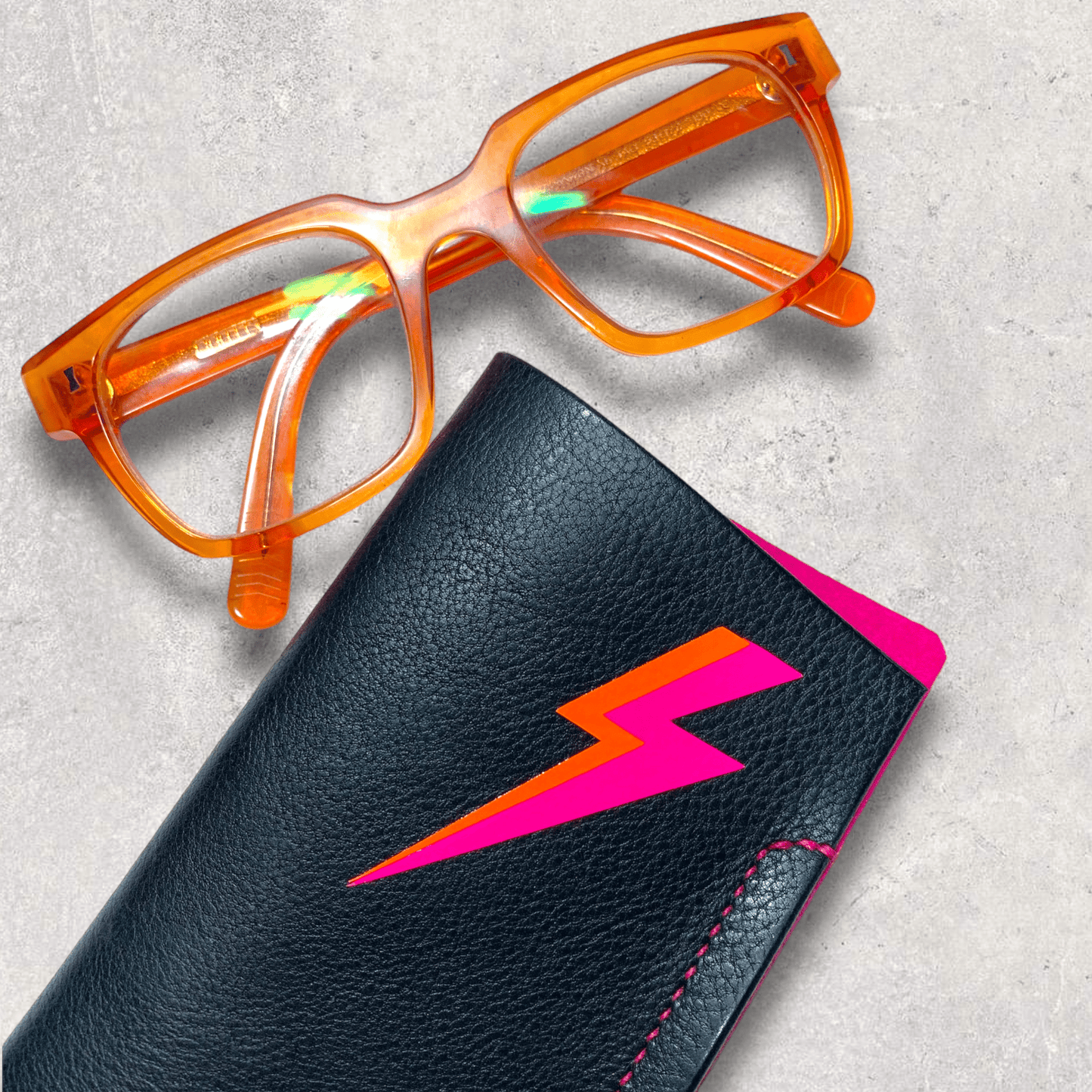 Black leather glasses case with pink felt lining and neon lightening bolt