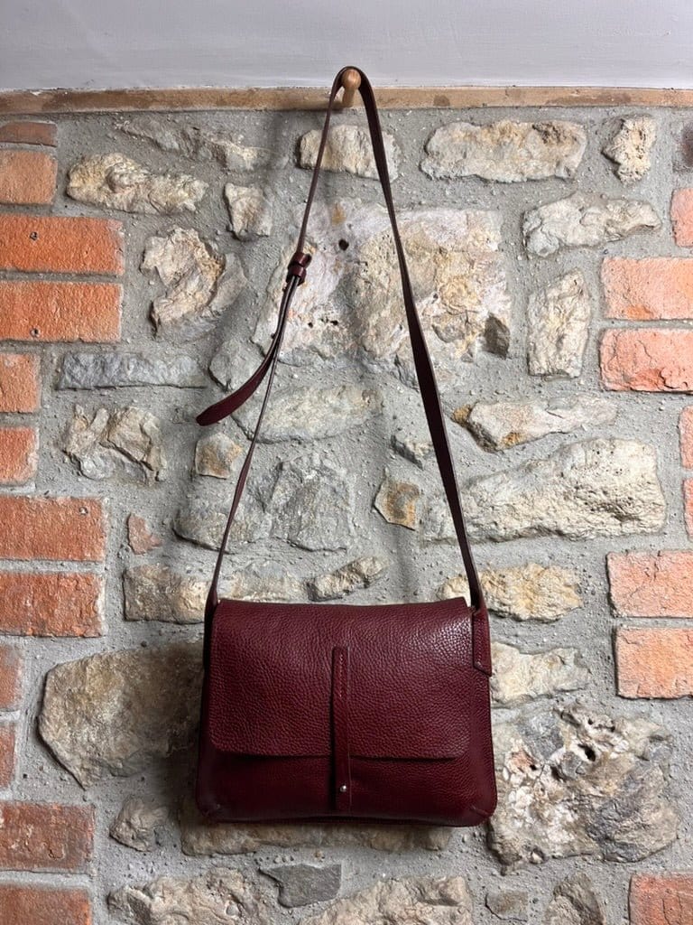 Burgundy barton bag hanging against a stone wall