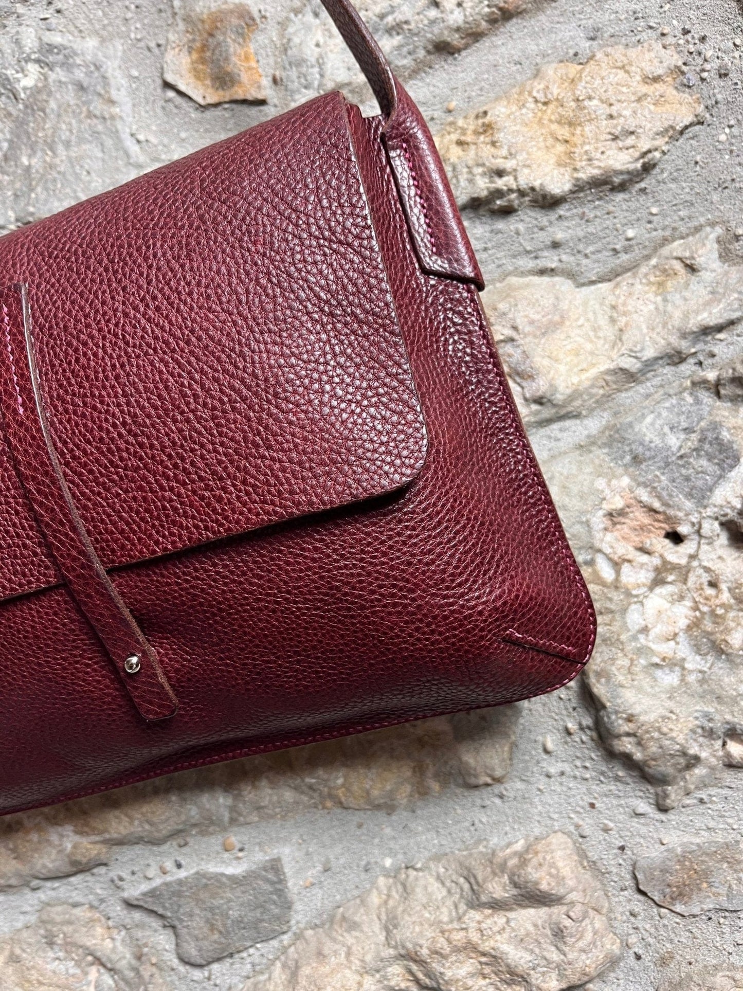 Close up detail of the barton bag in burgundy against a stone wall 