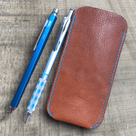 Beautiful dark tan leather pen sleeve with royal blue stitching beside and blue and silver pencil.